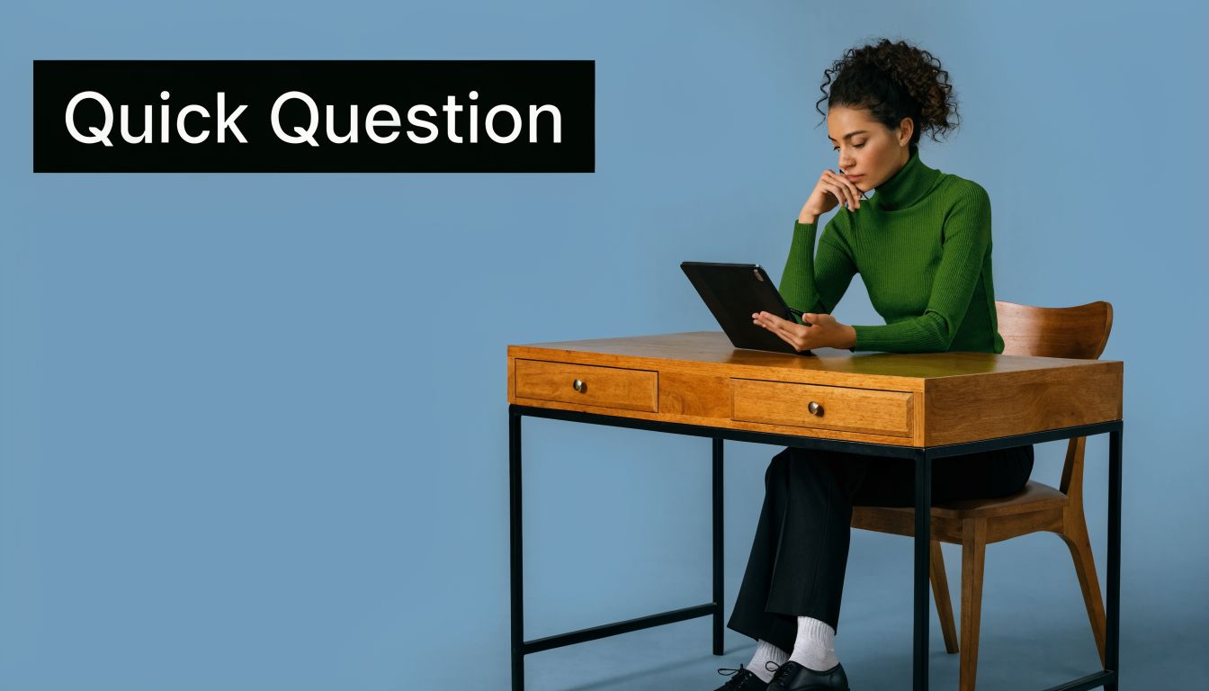 A woman in a green turtleneck sitting at a wooden desk while reviewing a tablet screen.